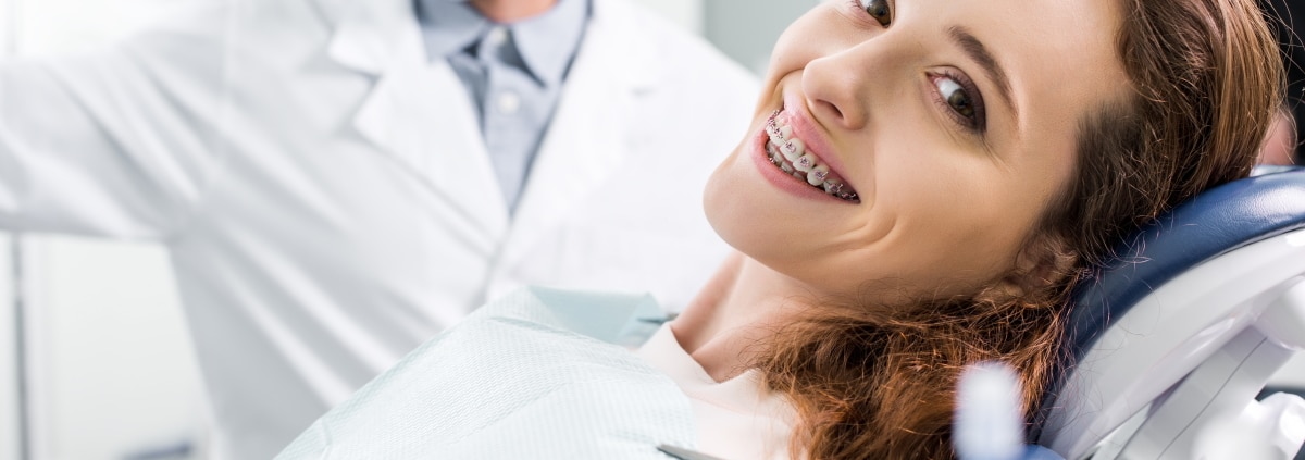 Eine Frau liegt auf dem Zahnarztstuhl und lächelt mit einer festen Zahnspange