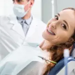 Eine Frau liegt auf dem Zahnarztstuhl und lächelt mit einer festen Zahnspange
