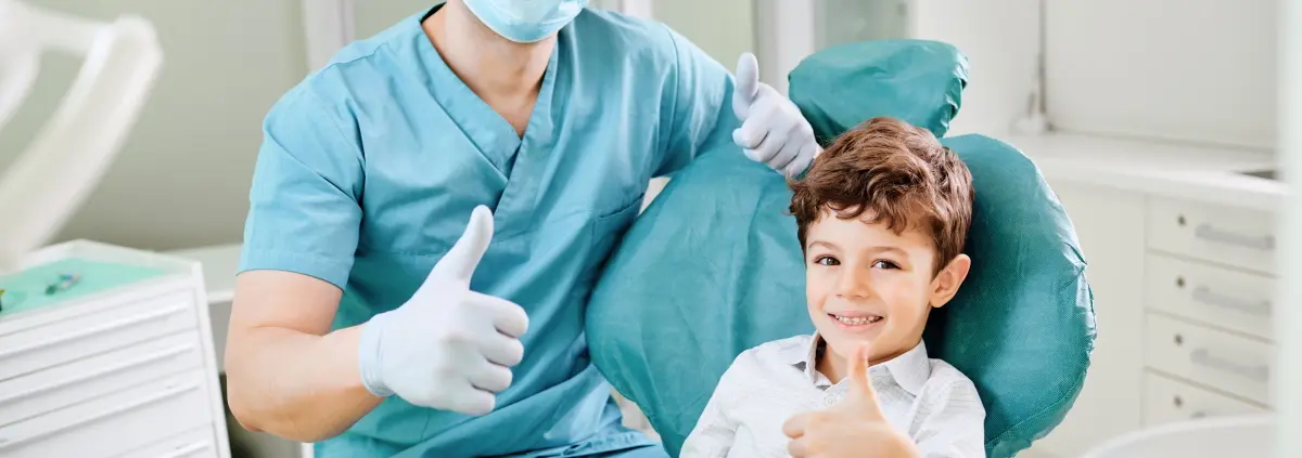 Kind und Kieferorthopäde zeigen mit dem Daumen nach oben und lächeln