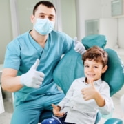 Kind und Kieferorthopäde zeigen mit dem Daumen nach oben und lächeln