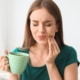 Junge Frau mit Kaffee in den Händen fasst sich an die Wange aufgrund von Zahnspangenschmerzen