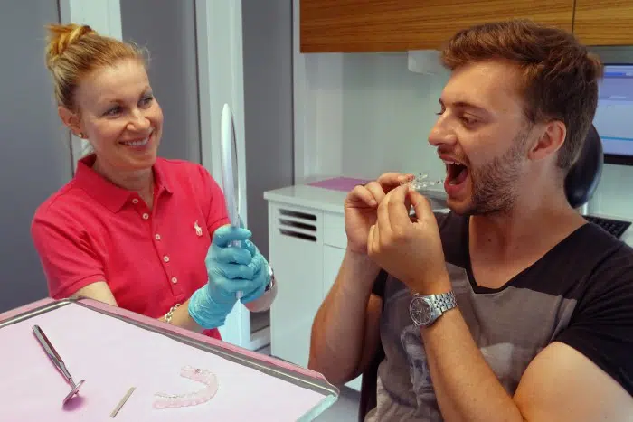 beim Behandlungsbeginn setzt der Patient seine erste Invisalign-Zahnschiene ein, die Kieferorthopädin unterstützt den Patienten dabei