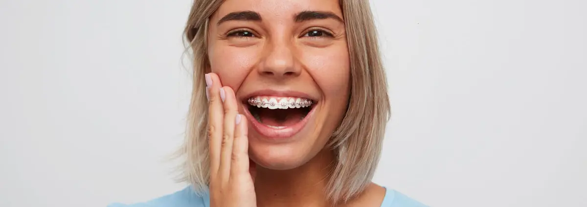 erwachsene Frau lächelt mit Zahnspange mit Metallbrackets und pinken Gummis