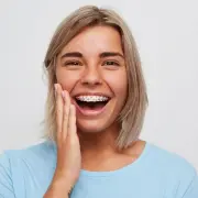 erwachsene Frau lächelt mit Zahnspange mit Metallbrackets und pinken Gummis