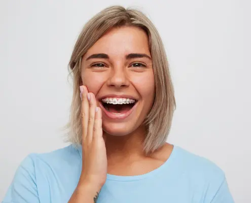 erwachsene Frau lächelt mit Zahnspange mit Metallbrackets und pinken Gummis
