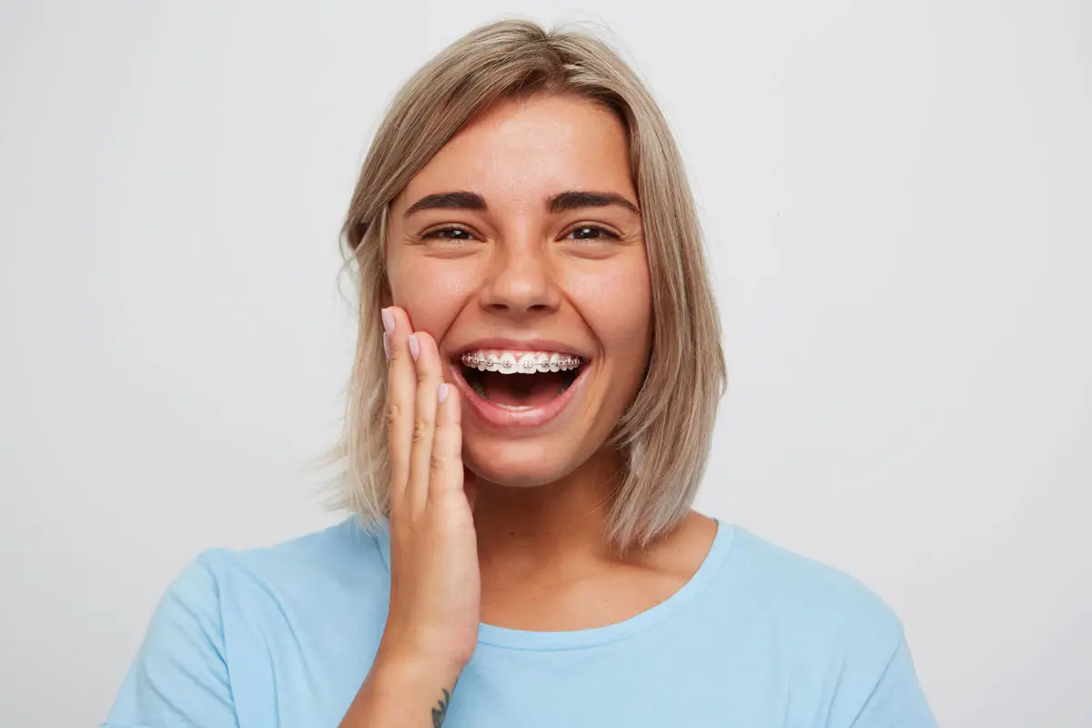 erwachsene Frau lächelt mit Zahnspange mit Metallbrackets und pinken Gummis