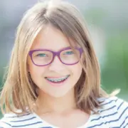 blondes Kind mit lila-farbiger Brille und einer festen Zahnspange mit blauen Gummis